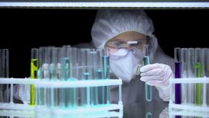 Scienziato guarda una provetta all'interno di un laboratorio con molte provette di colori diverso intorno