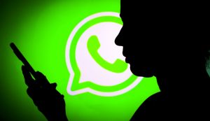 L'ombra di una persona con un telefono in mano davanti al logo di WhatsApp